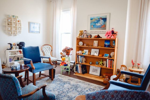 brightly lit counselling room with chairs and a wooden shelf